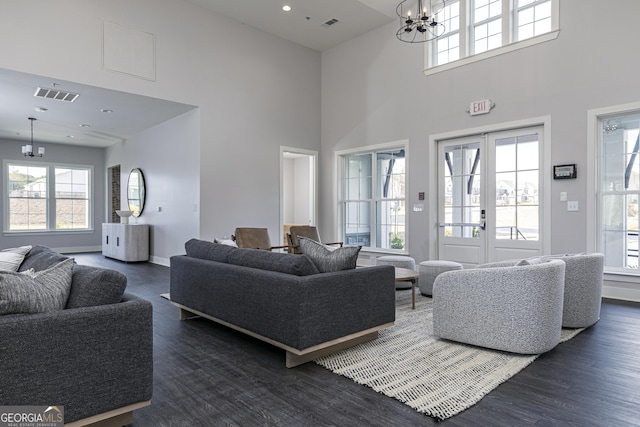 living room featuring a towering ceiling, dark wood-type flooring, an inviting chandelier, and a healthy amount of sunlight