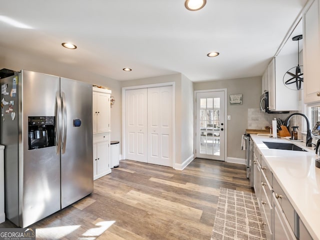 kitchen with sink, light hardwood / wood-style flooring, appliances with stainless steel finishes, white cabinetry, and tasteful backsplash