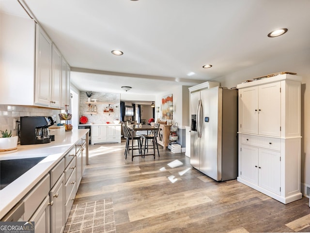 kitchen featuring backsplash, light wood-type flooring, white cabinets, and stainless steel refrigerator with ice dispenser