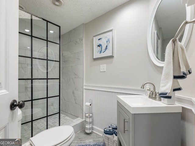 bathroom with vanity, a tile shower, a textured ceiling, and toilet