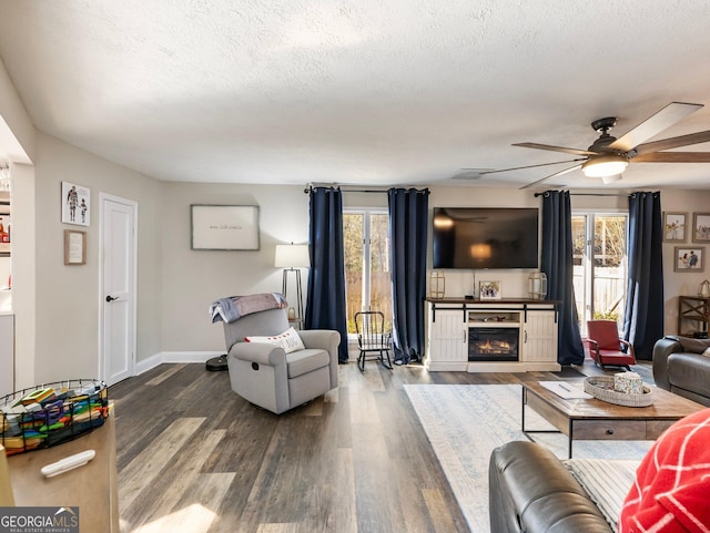 living room featuring ceiling fan, a textured ceiling, a fireplace, and wood-type flooring