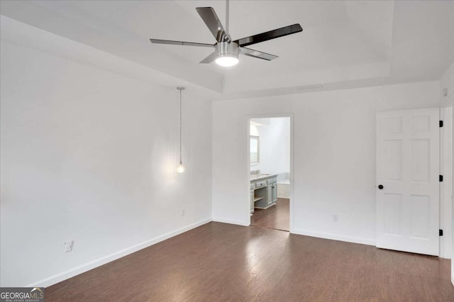 empty room featuring ceiling fan, a tray ceiling, and dark wood-type flooring