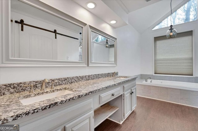 bathroom with lofted ceiling, wood-type flooring, tiled tub, and vanity