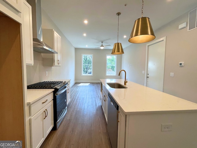 kitchen with a center island with sink, stainless steel appliances, wall chimney exhaust hood, sink, and decorative light fixtures