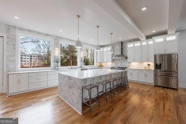 kitchen with white cabinets, stainless steel fridge with ice dispenser, and wall chimney range hood