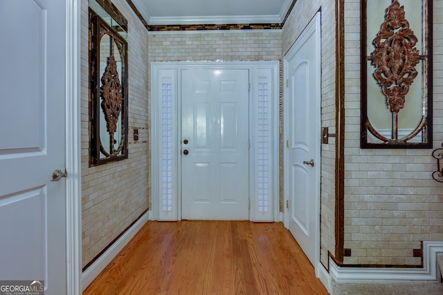 foyer with brick wall, light hardwood / wood-style floors, and crown molding