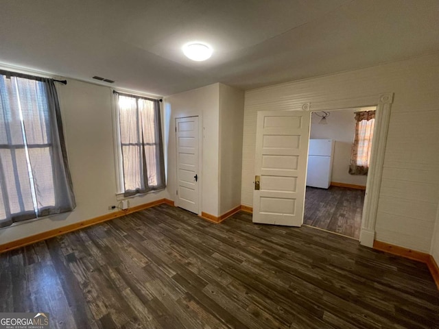 unfurnished bedroom featuring white fridge, a closet, multiple windows, and dark hardwood / wood-style floors