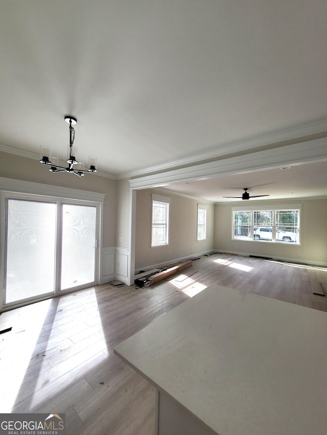 interior space with wainscoting, ornamental molding, light wood-type flooring, and a notable chandelier