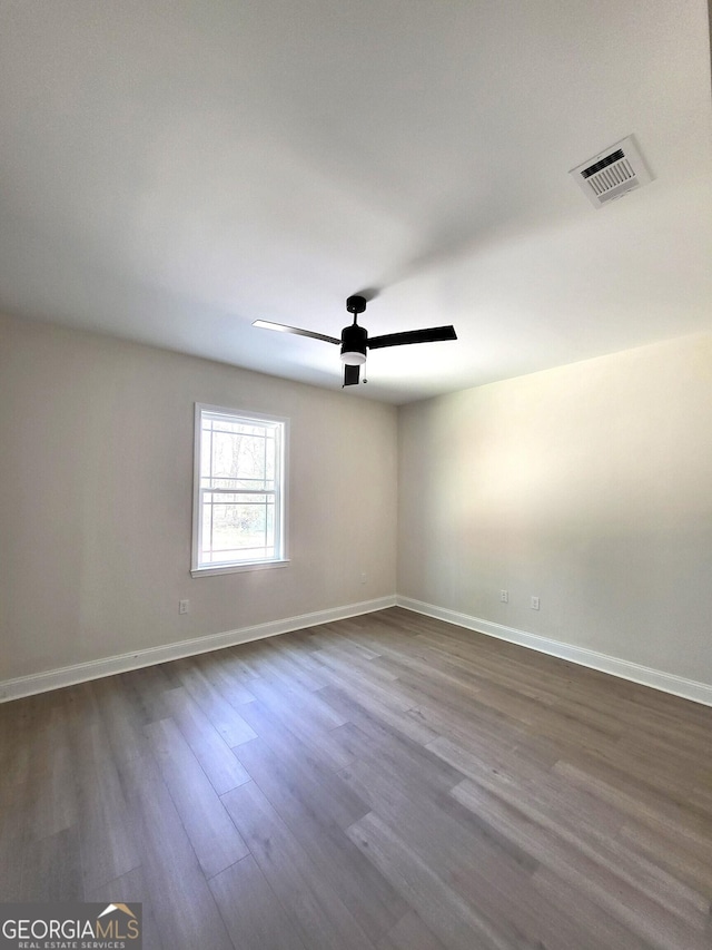 spare room featuring dark wood-type flooring, a ceiling fan, visible vents, and baseboards