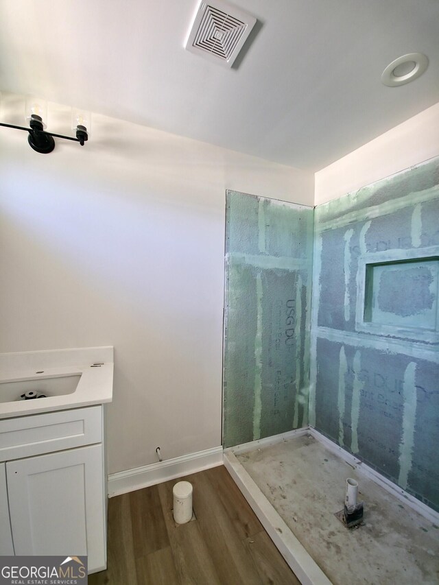 bathroom with visible vents, vanity, wood finished floors, baseboards, and walk in shower