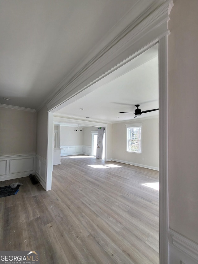 interior space with light wood-type flooring, ornamental molding, a ceiling fan, and wainscoting