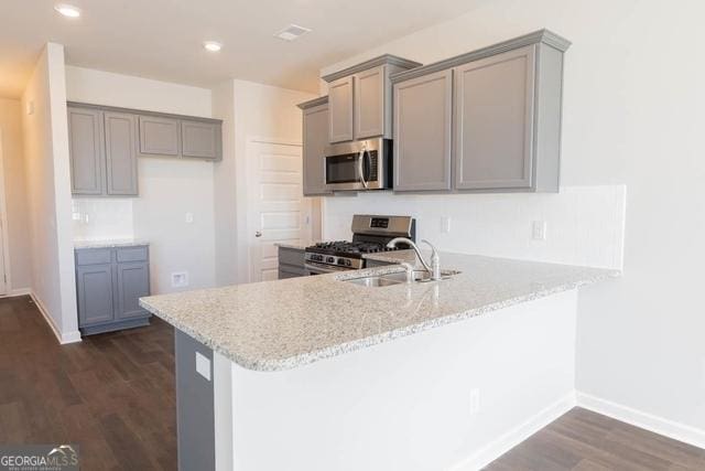 kitchen with sink, appliances with stainless steel finishes, kitchen peninsula, gray cabinetry, and dark wood-type flooring