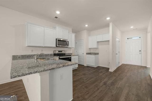 kitchen with stainless steel appliances, kitchen peninsula, light stone counters, white cabinets, and sink