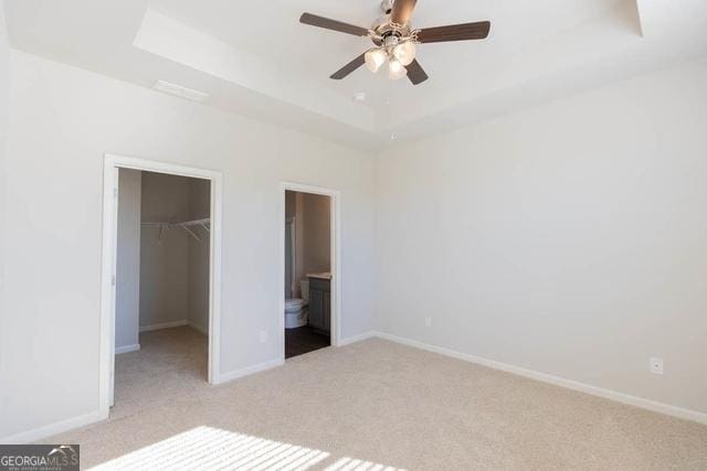 unfurnished bedroom with a walk in closet, a raised ceiling, a closet, and connected bathroom