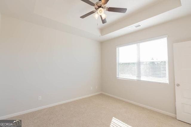 empty room featuring a raised ceiling, ceiling fan, and light carpet