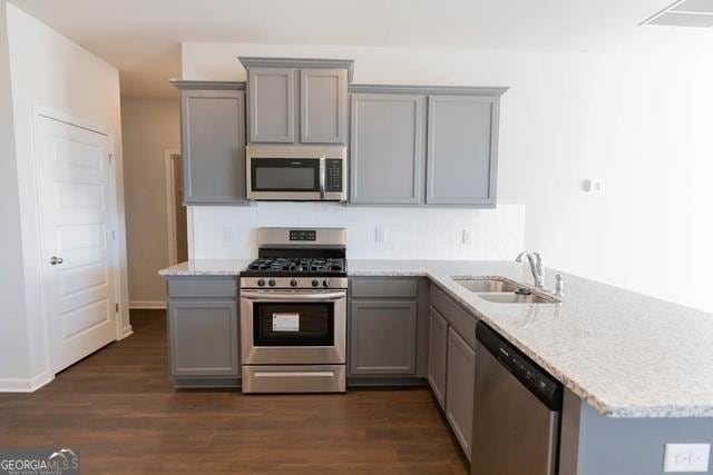 kitchen featuring stainless steel appliances, sink, light stone counters, kitchen peninsula, and gray cabinetry