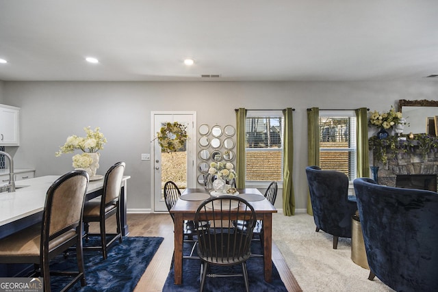 dining room with sink, hardwood / wood-style floors, and a stone fireplace