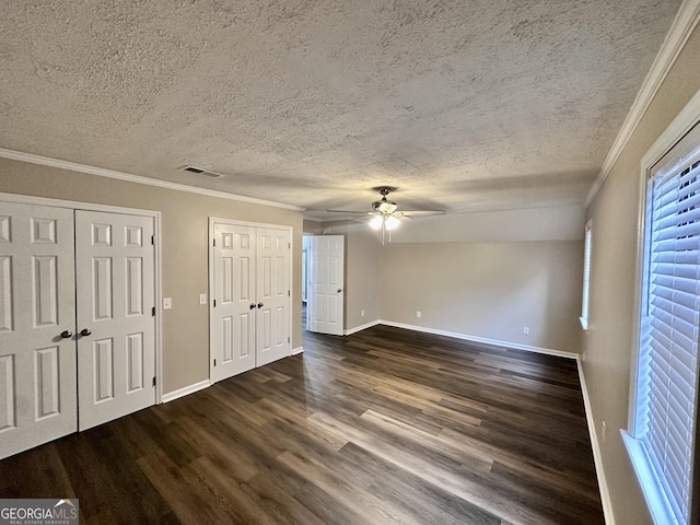 unfurnished bedroom featuring a textured ceiling, ornamental molding, two closets, and dark hardwood / wood-style floors