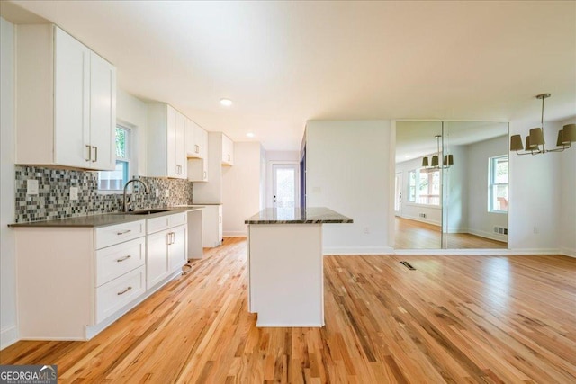 kitchen with tasteful backsplash, sink, white cabinets, and light wood-type flooring