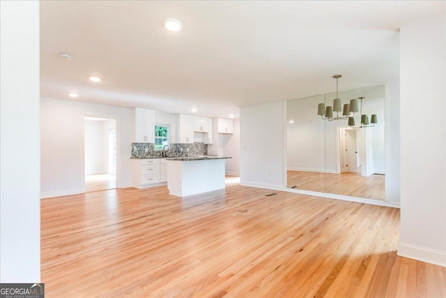 unfurnished living room with sink, a chandelier, and light hardwood / wood-style floors