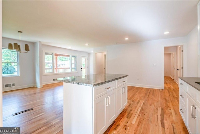 kitchen with pendant lighting, light hardwood / wood-style floors, white cabinets, a kitchen island, and dark stone counters