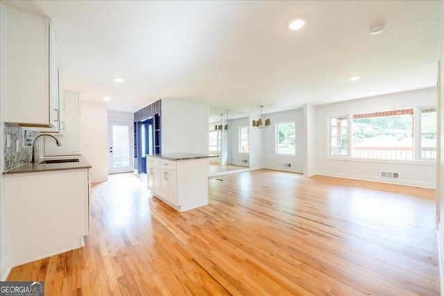 kitchen with sink, light hardwood / wood-style flooring, white cabinets, a kitchen island, and decorative backsplash