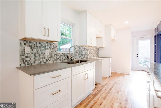 kitchen featuring backsplash, light wood-type flooring, sink, and white cabinets