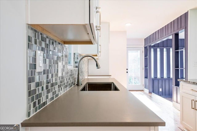 kitchen featuring tasteful backsplash, kitchen peninsula, sink, and white cabinets