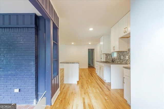 kitchen with sink, light hardwood / wood-style flooring, tasteful backsplash, white cabinets, and brick wall