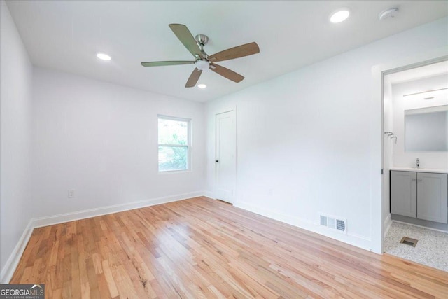 unfurnished bedroom featuring sink, light hardwood / wood-style flooring, ceiling fan, ensuite bath, and a closet