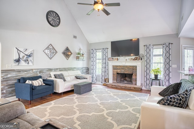 living room featuring high vaulted ceiling, dark hardwood / wood-style flooring, ceiling fan, and a stone fireplace