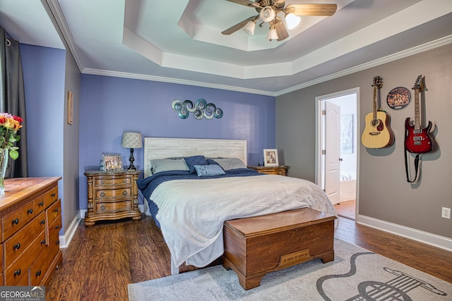 bedroom with dark hardwood / wood-style floors, connected bathroom, a tray ceiling, crown molding, and ceiling fan