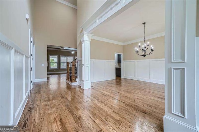 entryway featuring hardwood / wood-style floors, ceiling fan with notable chandelier, crown molding, and ornate columns