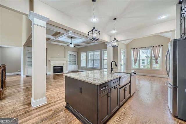 kitchen with light stone countertops, an island with sink, stainless steel fridge, ceiling fan, and dark brown cabinetry