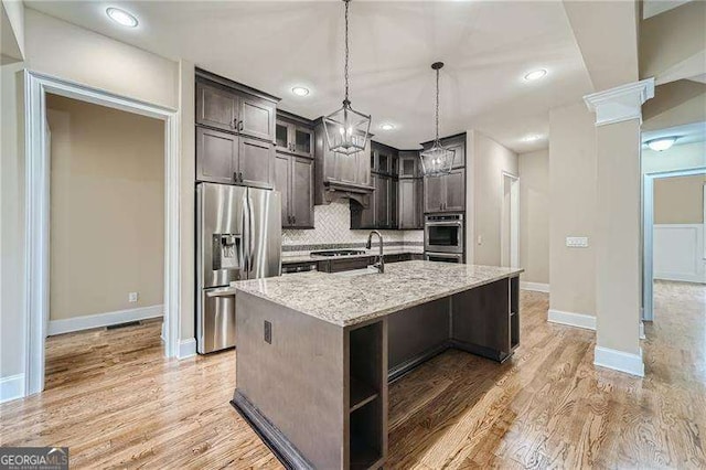 kitchen featuring dark brown cabinets, a kitchen island with sink, light stone counters, and appliances with stainless steel finishes