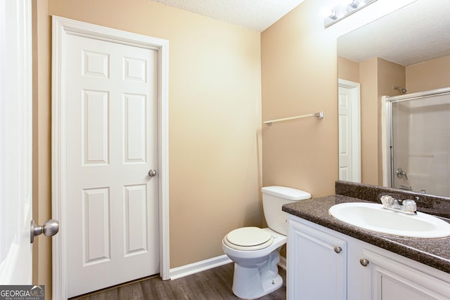 bathroom with toilet, wood-type flooring, vanity, a shower with shower door, and a textured ceiling