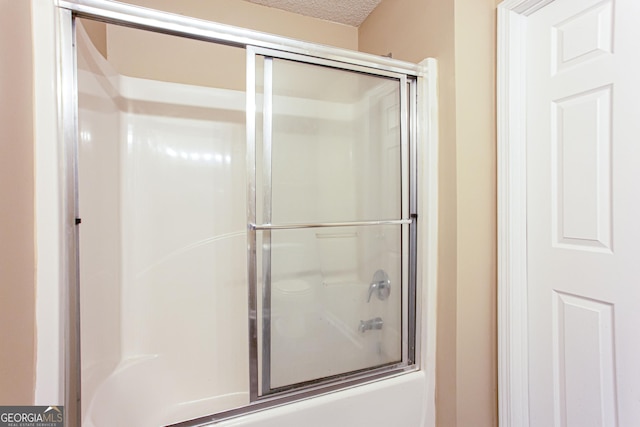 bathroom with combined bath / shower with glass door and a textured ceiling