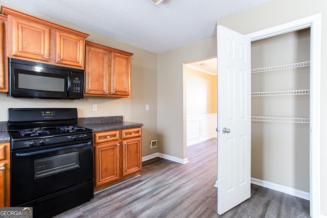 kitchen featuring a textured ceiling, ornamental molding, black appliances, and dark wood-type flooring