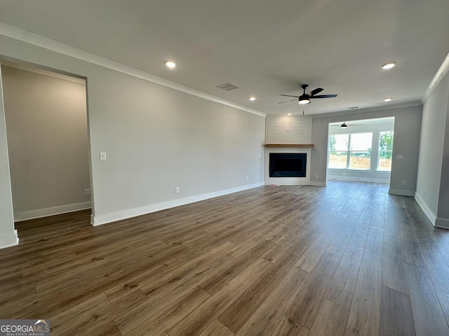 unfurnished living room with ceiling fan, a fireplace, dark wood-type flooring, visible vents, and ornamental molding