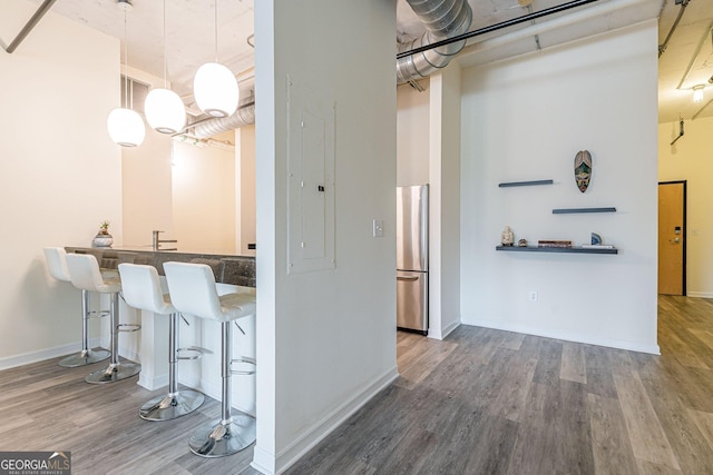 kitchen with a breakfast bar area, hanging light fixtures, stainless steel fridge, dark hardwood / wood-style flooring, and a high ceiling