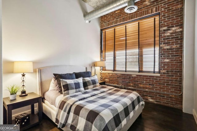 bedroom featuring brick wall and dark wood-type flooring