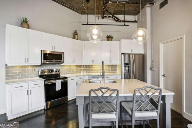 kitchen featuring pendant lighting, stainless steel appliances, a center island with sink, white cabinetry, and sink