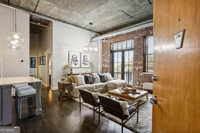 living room featuring a high ceiling, dark hardwood / wood-style flooring, a notable chandelier, and brick wall