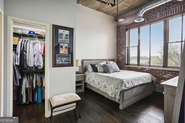 bedroom featuring brick wall, dark wood-type flooring, and a closet