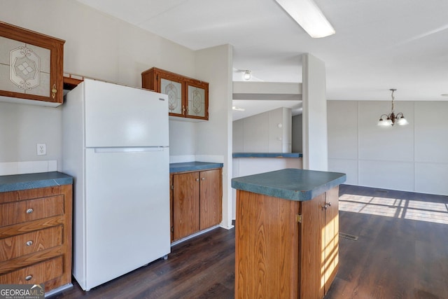 kitchen with a chandelier, hanging light fixtures, white refrigerator, dark wood-type flooring, and a kitchen island