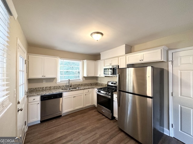 kitchen with stainless steel appliances, white cabinetry, sink, and light stone countertops