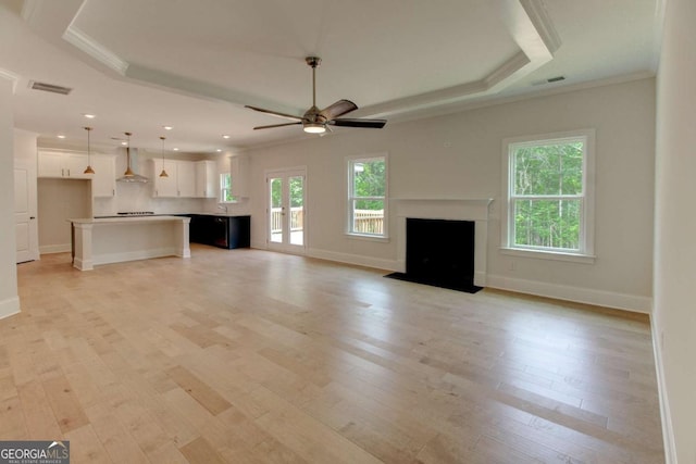 unfurnished living room with light wood finished floors, visible vents, a raised ceiling, a fireplace with flush hearth, and crown molding