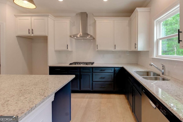 kitchen with light wood-style floors, appliances with stainless steel finishes, wall chimney range hood, white cabinetry, and a sink