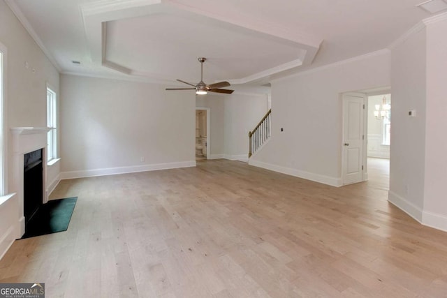 unfurnished living room with a fireplace, stairs, ornamental molding, light wood finished floors, and a raised ceiling