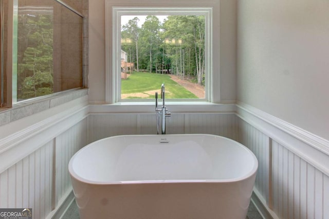 bathroom featuring a soaking tub, wainscoting, and plenty of natural light